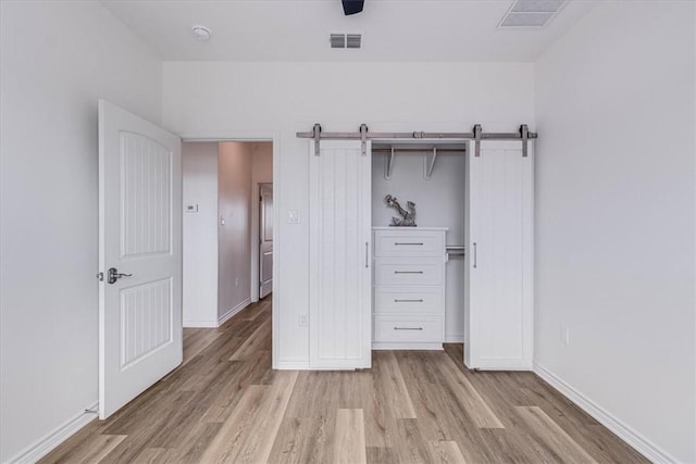 unfurnished bedroom with ceiling fan, a barn door, light hardwood / wood-style floors, and a closet