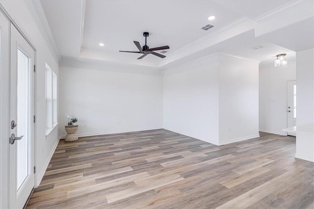 spare room with ornamental molding, ceiling fan, light hardwood / wood-style floors, a raised ceiling, and a healthy amount of sunlight