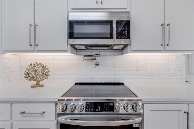 kitchen with stainless steel appliances, tasteful backsplash, white cabinets, and light stone counters