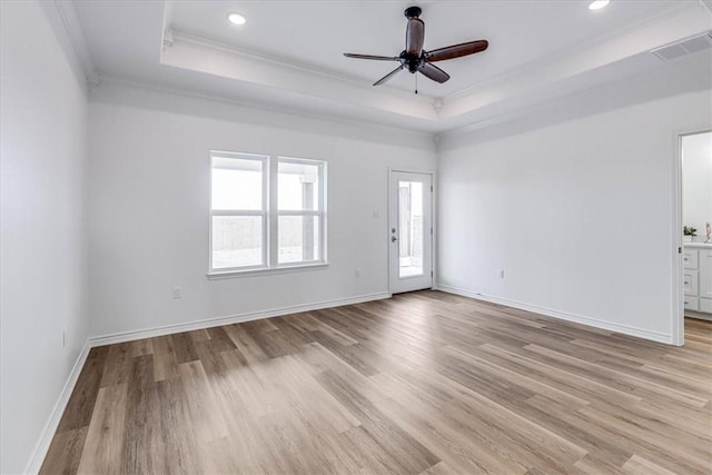 empty room featuring a raised ceiling, ornamental molding, ceiling fan, and light wood-type flooring