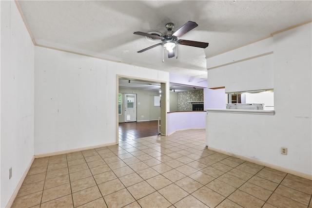 tiled empty room featuring a fireplace, ceiling fan, a textured ceiling, and a healthy amount of sunlight