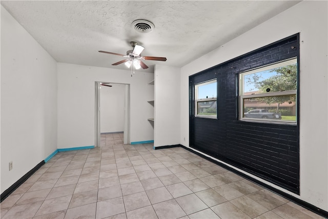 empty room featuring a textured ceiling, light tile patterned floors, and ceiling fan