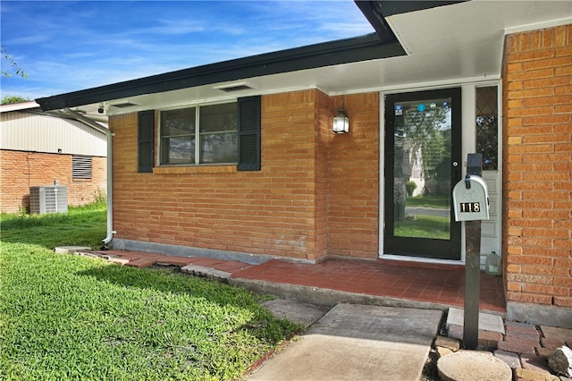 view of exterior entry with a lawn and cooling unit