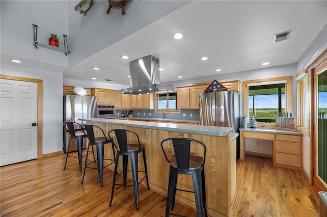 178 Smyth St, Port Oconnor, TX 77982 - kitchen with island exhaust hood, stainless steel appliances, light wood-style flooring, light brown cabinetry, and recessed lighting