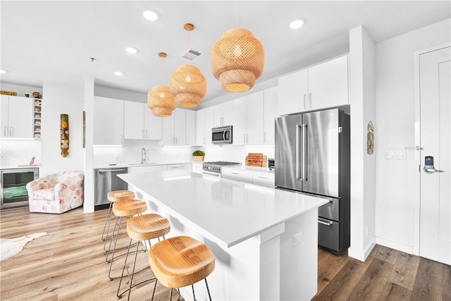 kitchen with stainless steel appliances, hardwood / wood-style flooring, white cabinetry, and pendant lighting