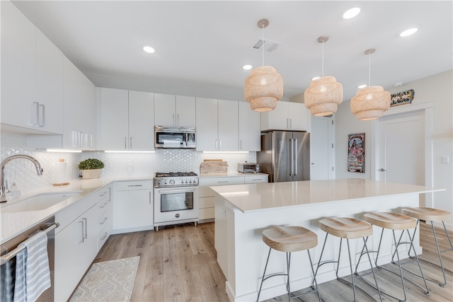 kitchen featuring white cabinetry, sink, light hardwood / wood-style flooring, premium appliances, and pendant lighting