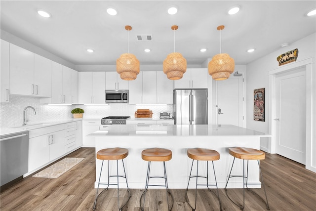 kitchen with pendant lighting, white cabinetry, appliances with stainless steel finishes, and wood-type flooring