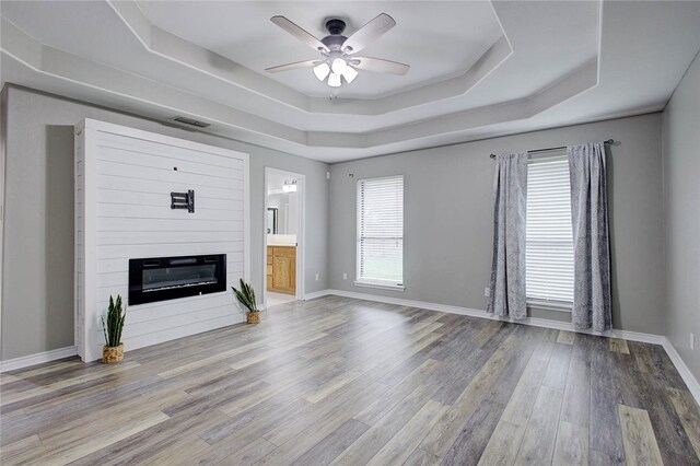 unfurnished living room with hardwood / wood-style floors, ceiling fan, and a raised ceiling