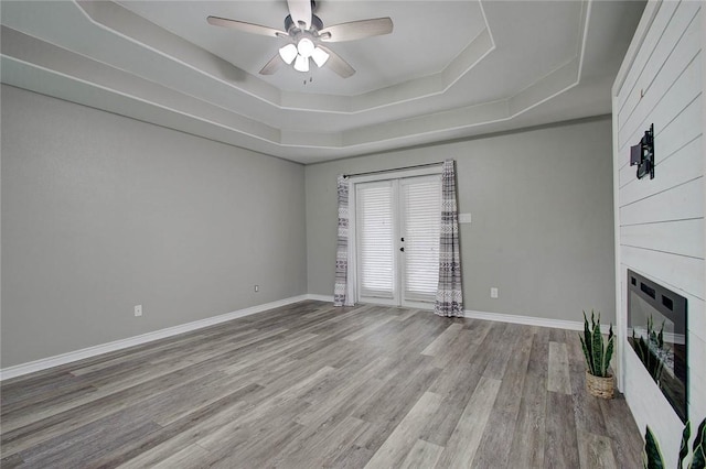 2111 Buckeye Dr, Ingleside, TX 78362 - unfurnished living room featuring a tray ceiling, wood finished floors, a large fireplace, ceiling fan, and baseboards