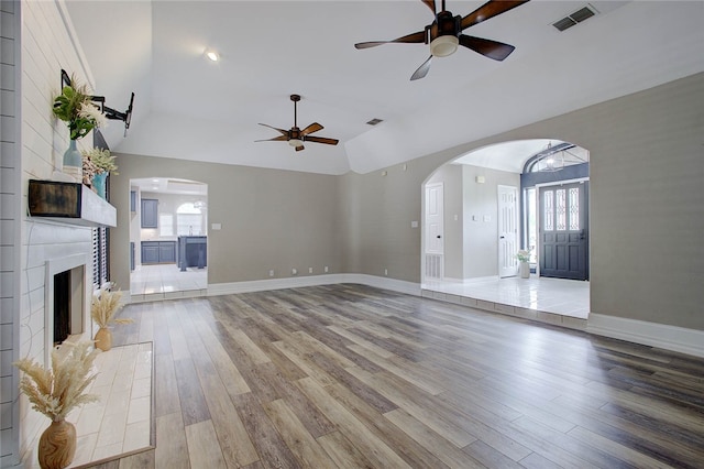 unfurnished living room with a large fireplace, wood-type flooring, ceiling fan, and lofted ceiling