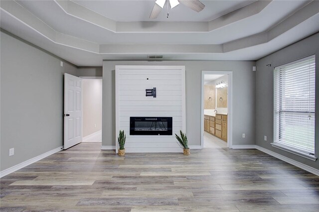 unfurnished living room featuring ceiling fan, a raised ceiling, and light hardwood / wood-style flooring