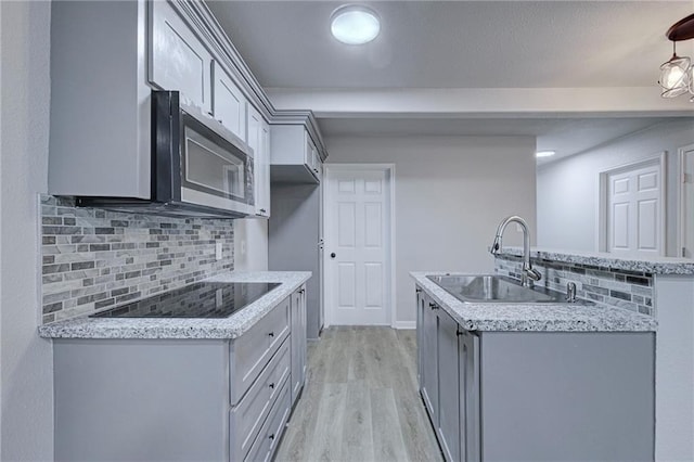 kitchen featuring black electric stovetop, a sink, decorative backsplash, light wood finished floors, and stainless steel microwave