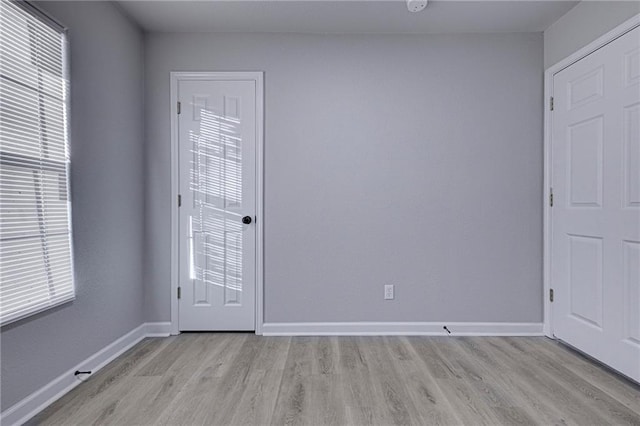 unfurnished room with light wood finished floors, plenty of natural light, and baseboards