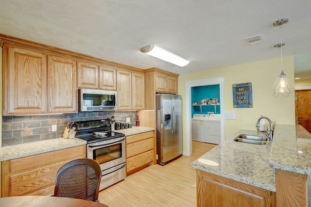 kitchen featuring light stone countertops, appliances with stainless steel finishes, sink, independent washer and dryer, and hanging light fixtures