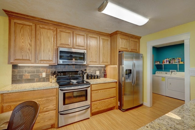 kitchen featuring washer and dryer, decorative backsplash, stainless steel appliances, and light stone countertops