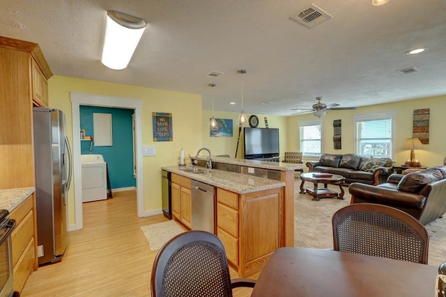 kitchen with pendant lighting, sink, light stone countertops, appliances with stainless steel finishes, and washer / clothes dryer