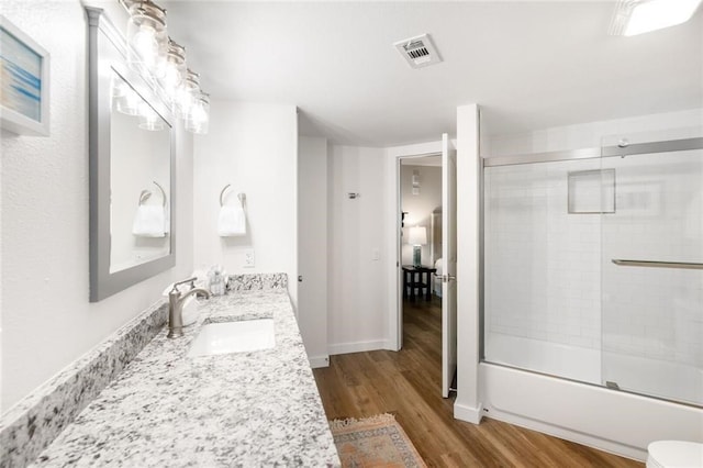 full bathroom with hardwood / wood-style floors, enclosed tub / shower combo, toilet, and vanity