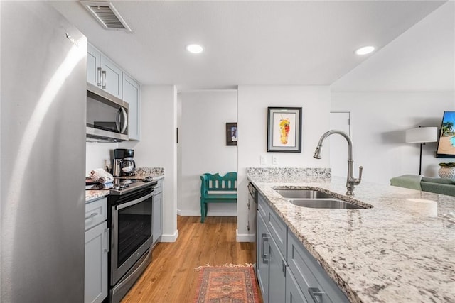 kitchen with stainless steel appliances, light stone countertops, sink, and light wood-type flooring