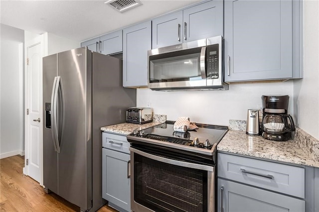 kitchen with gray cabinetry, light stone countertops, appliances with stainless steel finishes, and light hardwood / wood-style floors