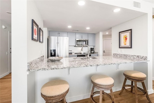 kitchen featuring stainless steel appliances, light hardwood / wood-style floors, gray cabinetry, and kitchen peninsula