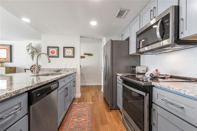 kitchen with stainless steel appliances, light hardwood / wood-style floors, sink, light stone counters, and gray cabinets