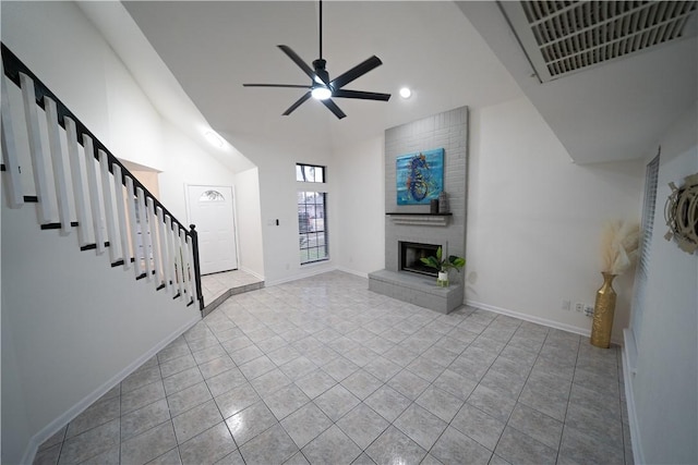 unfurnished living room featuring ceiling fan, a towering ceiling, light tile patterned floors, and a fireplace