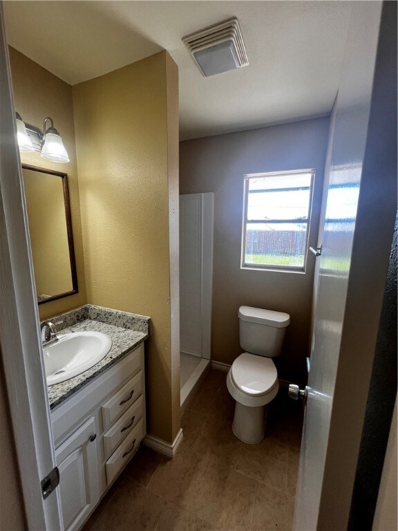 bathroom featuring walk in shower, vanity, toilet, and tile patterned flooring