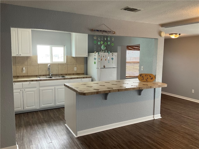 kitchen featuring wood counters, decorative backsplash, white refrigerator, white cabinets, and sink