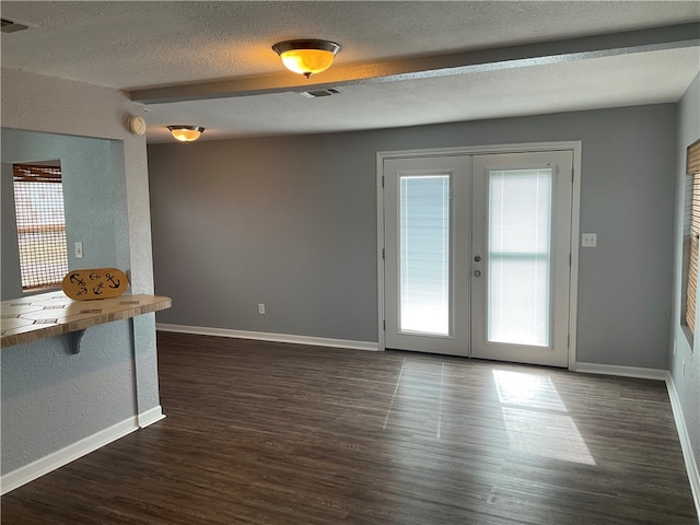 unfurnished living room with a textured ceiling, dark hardwood / wood-style floors, and french doors