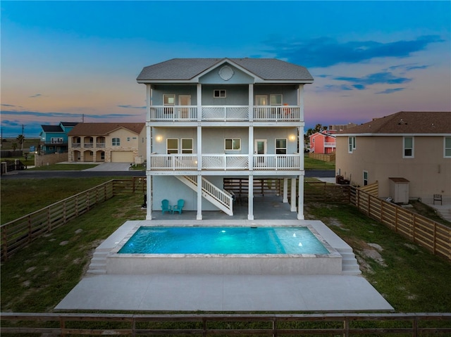 back house at dusk with a swimming pool with hot tub, a balcony, and a patio area