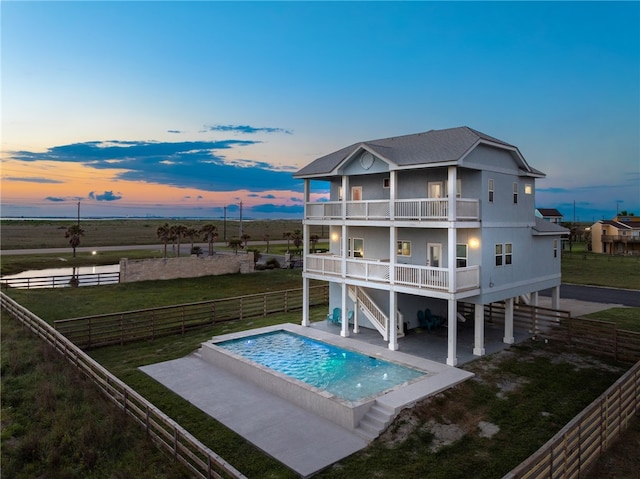 back house at dusk featuring a lawn, a balcony, a fenced in pool, and a patio