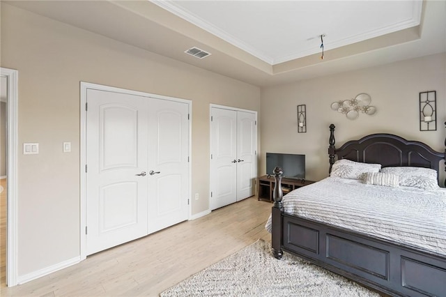 bedroom with multiple closets, light wood-style floors, a raised ceiling, baseboards, and crown molding