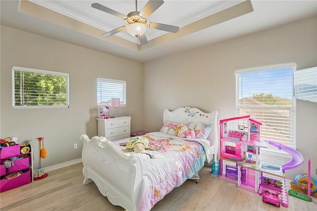 bedroom with a raised ceiling, hardwood / wood-style flooring, ornamental molding, ceiling fan, and baseboards