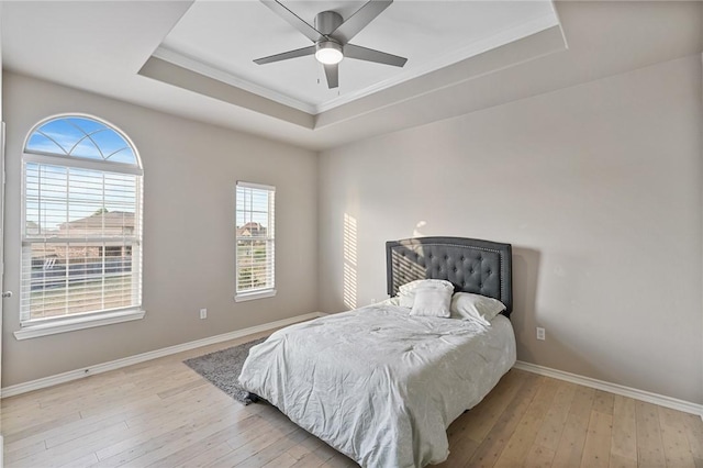 bedroom with a raised ceiling, light wood-style flooring, baseboards, crown molding, and ceiling fan
