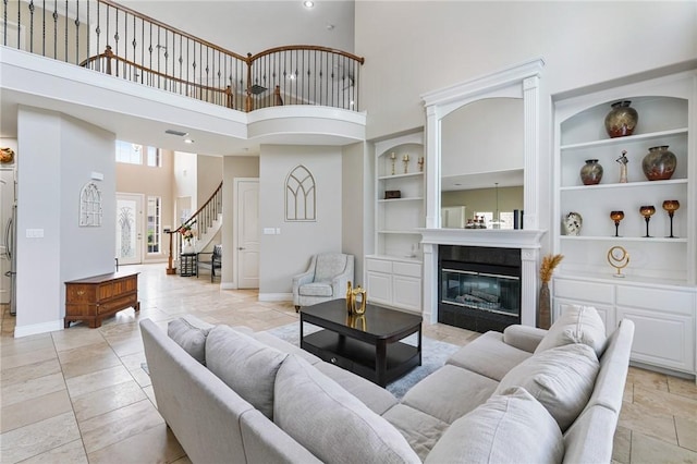 living area with a towering ceiling, built in features, stairs, a glass covered fireplace, and baseboards
