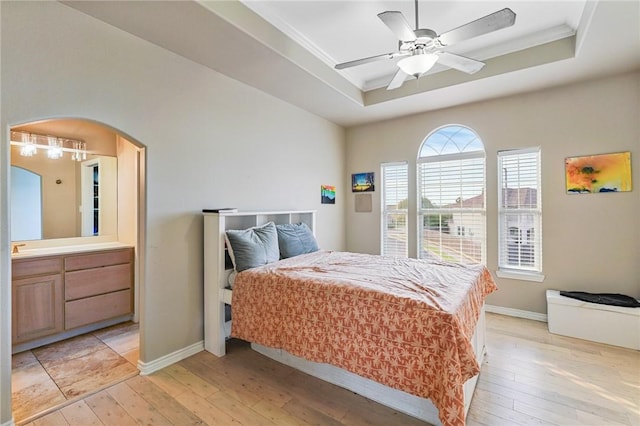 bedroom with a raised ceiling, light wood-type flooring, arched walkways, baseboards, and ceiling fan