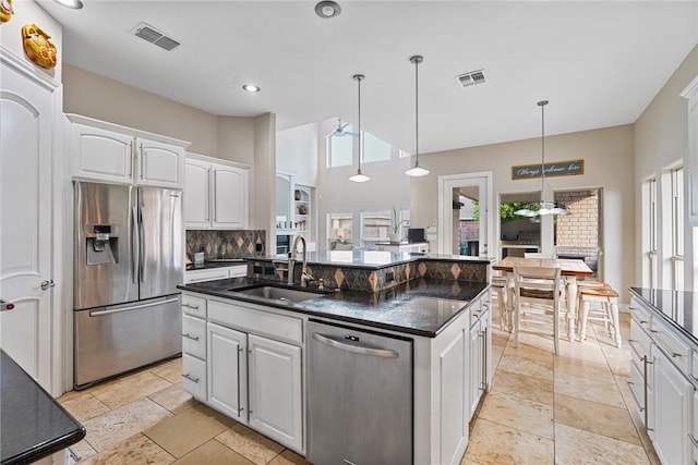 kitchen featuring appliances with stainless steel finishes, a sink, white cabinets, a center island with sink, and decorative backsplash