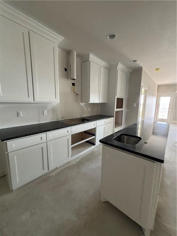 kitchen featuring dark countertops, a sink, white cabinetry, and concrete flooring