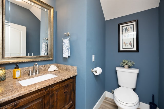 bathroom with hardwood / wood-style floors, lofted ceiling, toilet, and vanity