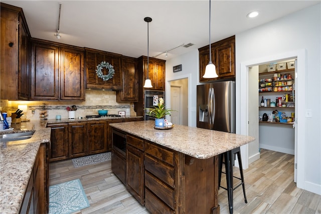 kitchen with stainless steel appliances, a center island, decorative light fixtures, and light wood-type flooring