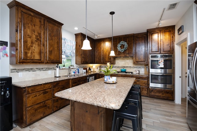 kitchen featuring light stone counters, light wood-type flooring, appliances with stainless steel finishes, hanging light fixtures, and a center island