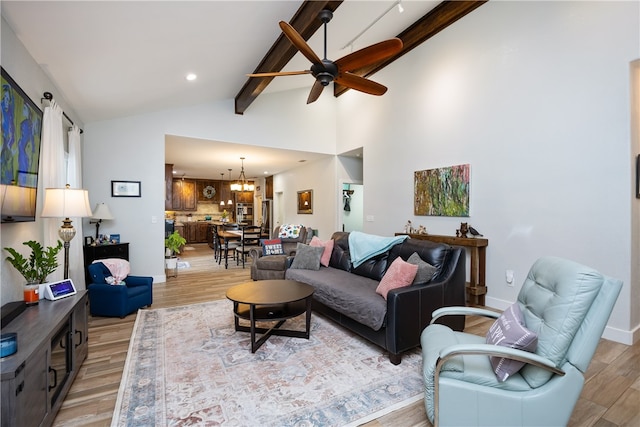 living room with light wood-type flooring, ceiling fan with notable chandelier, and vaulted ceiling with beams