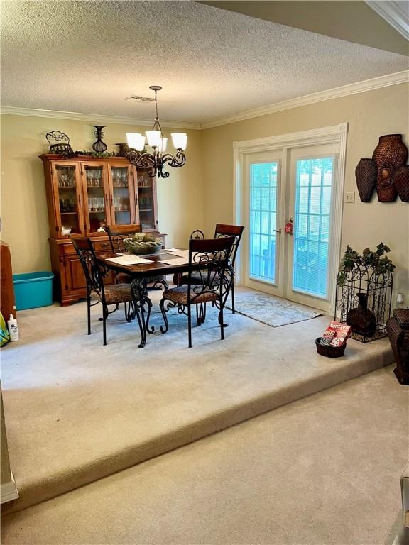 carpeted dining room featuring crown molding, a textured ceiling, and an inviting chandelier