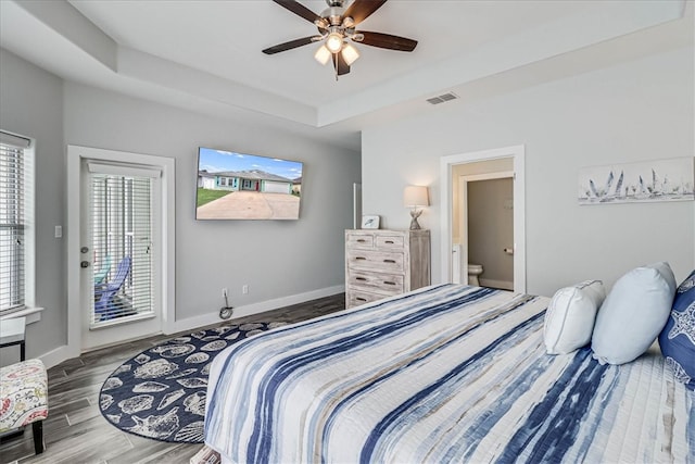 bedroom with ensuite bathroom, ceiling fan, hardwood / wood-style floors, a raised ceiling, and access to outside