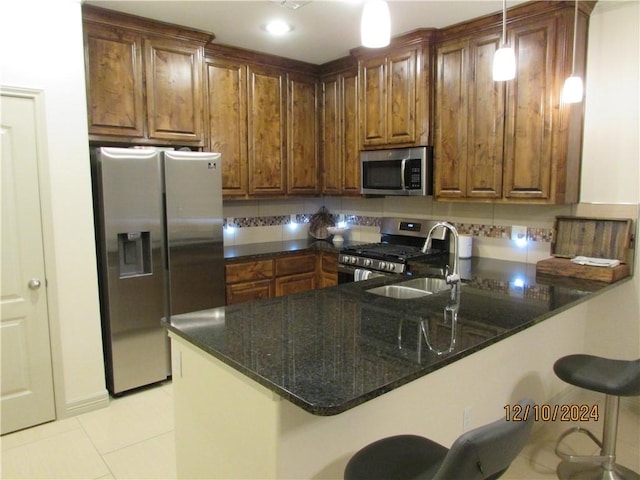 kitchen featuring kitchen peninsula, appliances with stainless steel finishes, a kitchen bar, sink, and decorative light fixtures