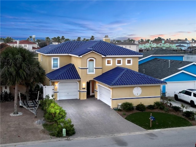 view of front of home featuring a tile roof, stucco siding, a chimney, decorative driveway, and a garage