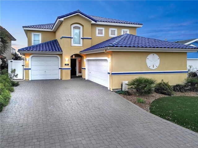 view of front of house featuring fence, a tiled roof, stucco siding, decorative driveway, and an attached garage