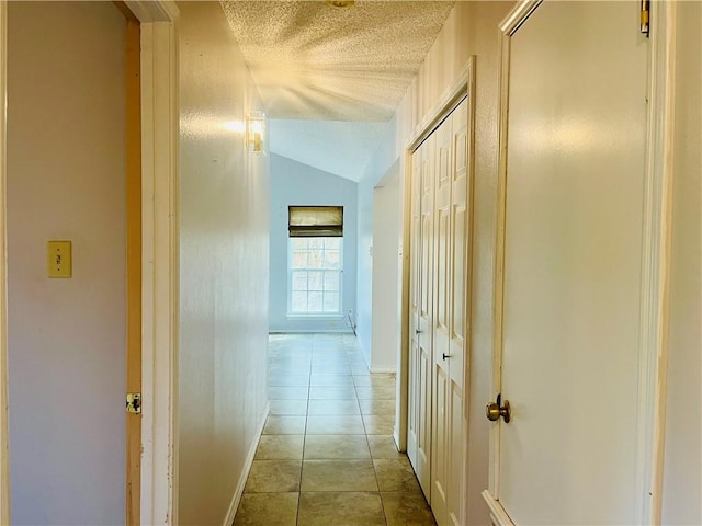 corridor with light tile patterned floors, a textured ceiling, and vaulted ceiling