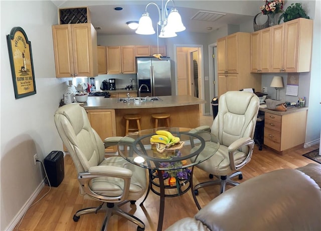 kitchen with light hardwood / wood-style floors, stainless steel fridge, light brown cabinets, decorative light fixtures, and sink