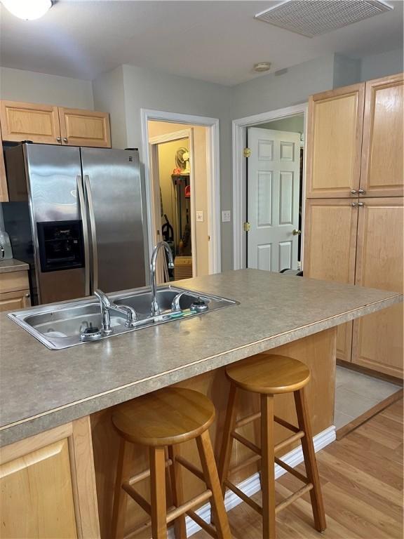 kitchen featuring stainless steel refrigerator with ice dispenser, a kitchen bar, light brown cabinets, sink, and light hardwood / wood-style flooring